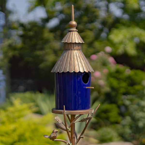 side view image of Iron and glossy cobalt blue porcelain birdhouse stake with ornate roof and a little bird perched on leaves attached to the stake