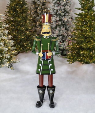Life-size iron Christmas nutcracker figure Leo in green holding drum in front of lighted up trees