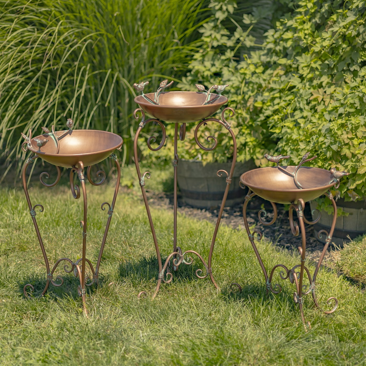 3 metal birdbaths in antique copper finish with birds and ornate stands in garden
