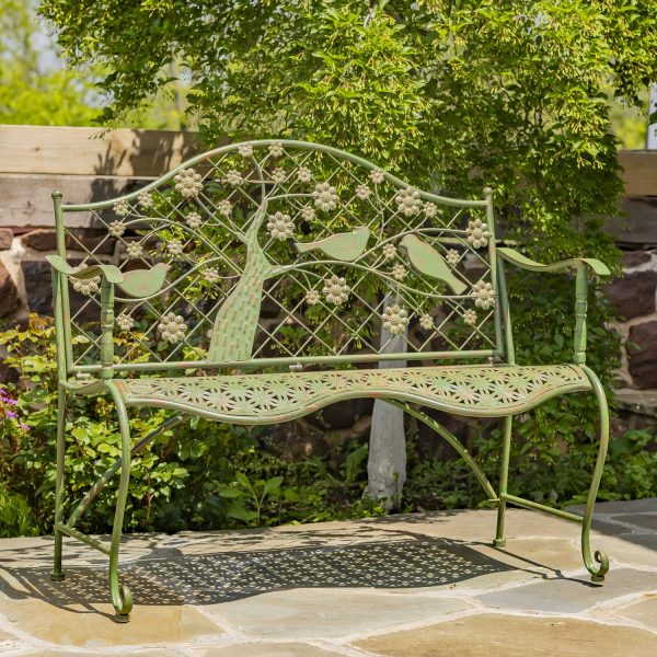 classic iron garden bench with blooming tree and birds on lattice backrest in distressed antique rust-green finish