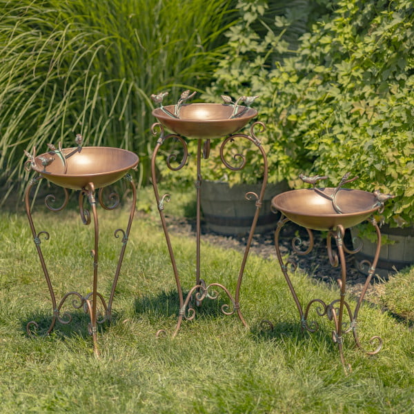 3 metal birdbaths in antique copper finish with birds and ornate stands in garden