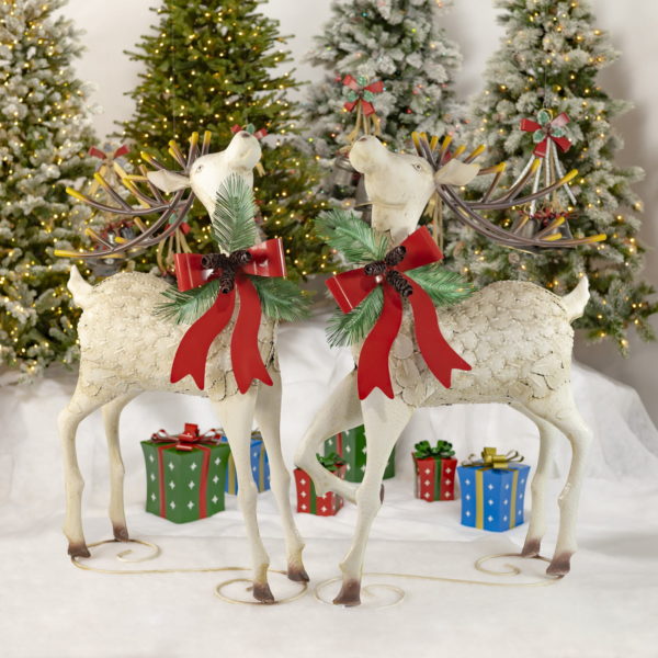 Two large white iron reindeer with pinecone bow watching upwards standing on a curlicue iron design