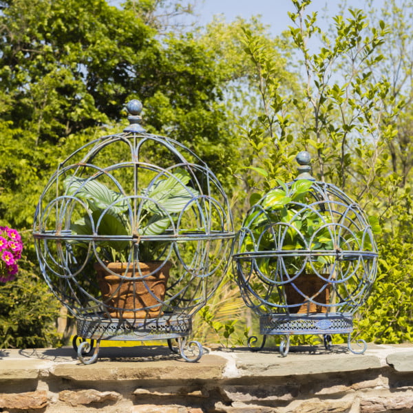 Set of 2 large and small iron globe plant stands in antique blue with plant pots inside on a fence