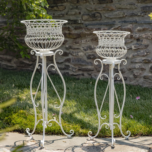 2 tall Victorian-style iron basket plant stands in antique white distressed finish in garden