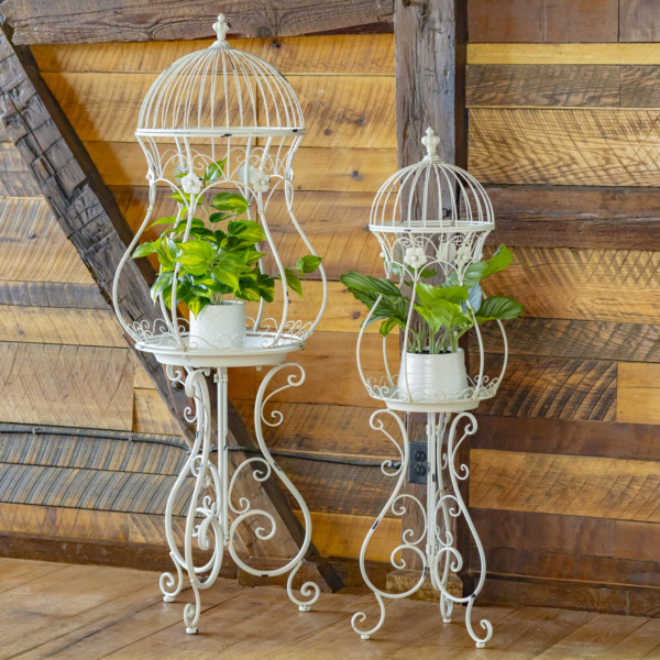 Two Metal Plant Stands shaped like an hour glass birdcage in Antique white with curlicue structure folding stands with plants inside (Plants not included)