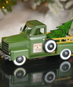 Small green iron truck with yellow bars to the back of the truck with christmas tree in the tray