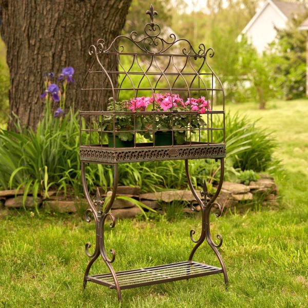 rectangular metal bird cage plant stand with fleur-de-lis details and shelf in antique bronze distressed finish with flower pots inside it