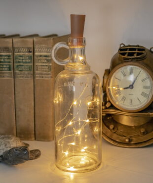 Bottle cork LED string lights inside clear wine bottle between old books turtle and diving helmet clock