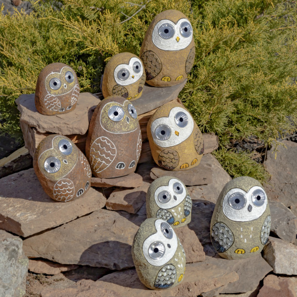 Nine Solar rock Owls sitting on some rocks with eyes that lit up in the dark in sets of three colors , natural brown, Tan Brown and grey with there feet and wings painted on to them