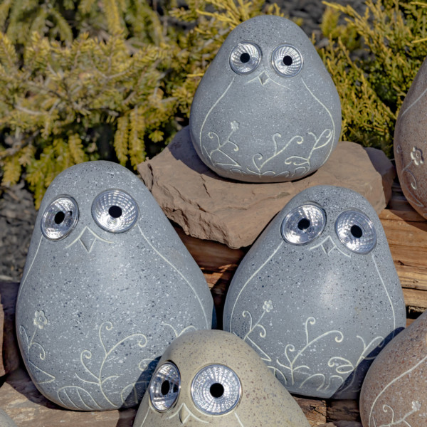 One set of three grey solar bird rocks with floral etching sitting on some rocks looking at you with there round big eyes that lights up in the dark