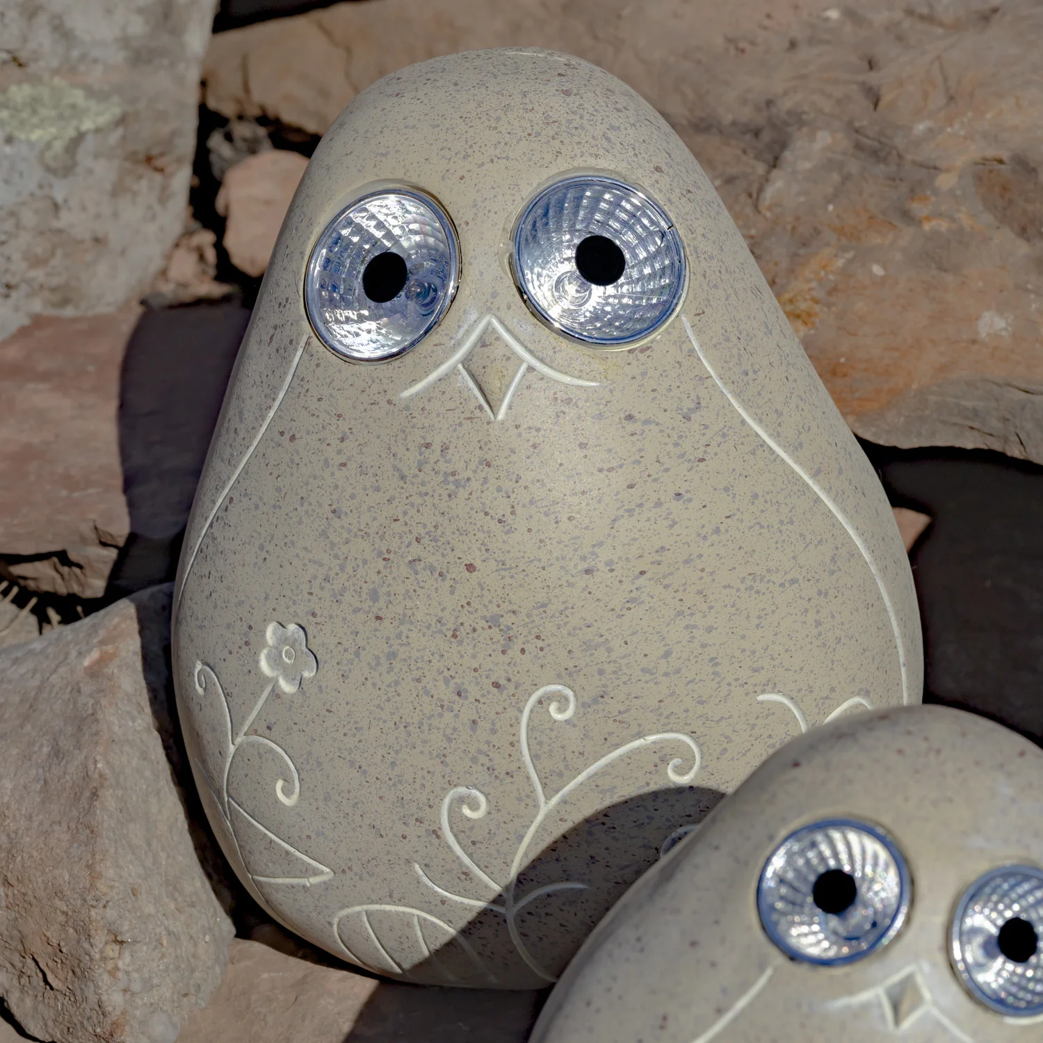 One large beige solar bird rock with floral etching sitting on some rocks looking at you with there big round eyes that lights up in the dark