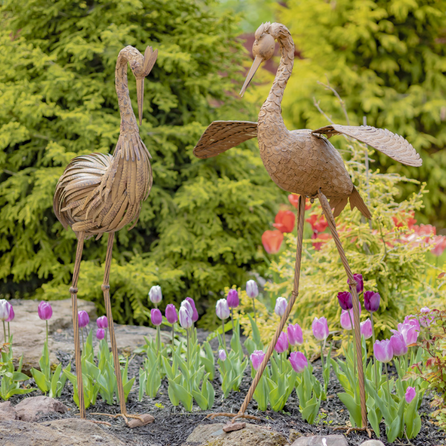 Two large brown rustic Herons standing tall looking down at the beautiful flowers ( Flowers not included )