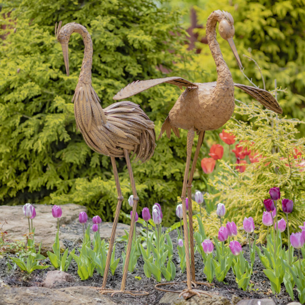 Two large brown rustic Herons standing tall looking down at the beautiful flowers ( Flowers not included )