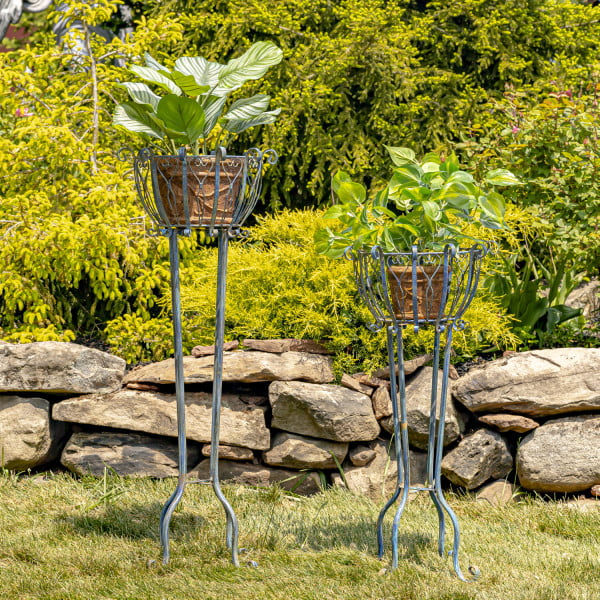 Set of 2 tall iron basket plant four-legged stands with heart-shaped details in distressed antique blue finish in garden with not included plant pots inside