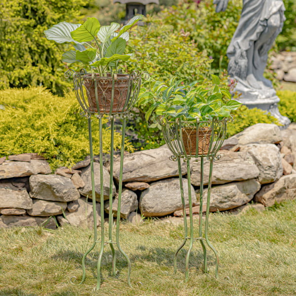 Set of 2 tall iron basket plant four-legged stands with heart-shaped details in distressed antique green finish in garden with not included plant pots inside