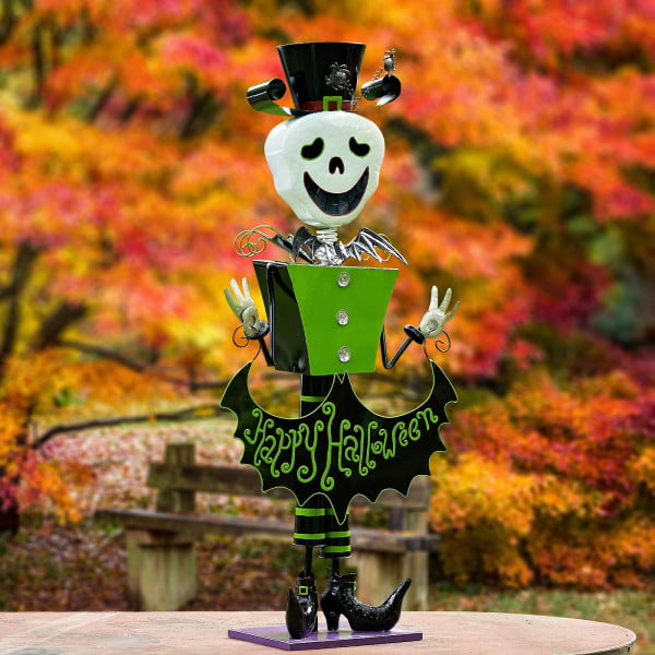 tall iron Halloween skeleton figurine in top hat holding Happy Halloween sign in fall forest
