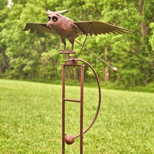 closeup of iron flying owl with flapping wings balanced on garden stake with ball anchor outside