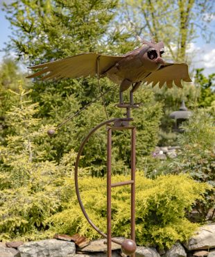 closeup of iron flying owl with flapping wings balanced on garden stake with ball anchor outside