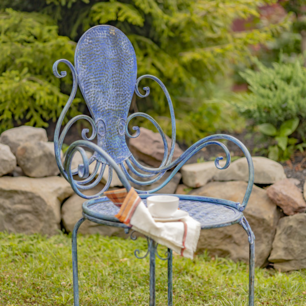 Close up image of A blue Coastal iron armchair with the backrest shaped like an Octopus and a tea cup is also rested on a saucer on the chair for additional décor - ( Teacup and saucer not included )