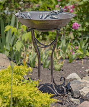 Tall bronze finish birdbath with two birds perched on either end of it with curlicue standing legs