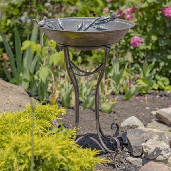 Tall bronze finish birdbath with two birds perched on either end of it with curlicue standing legs