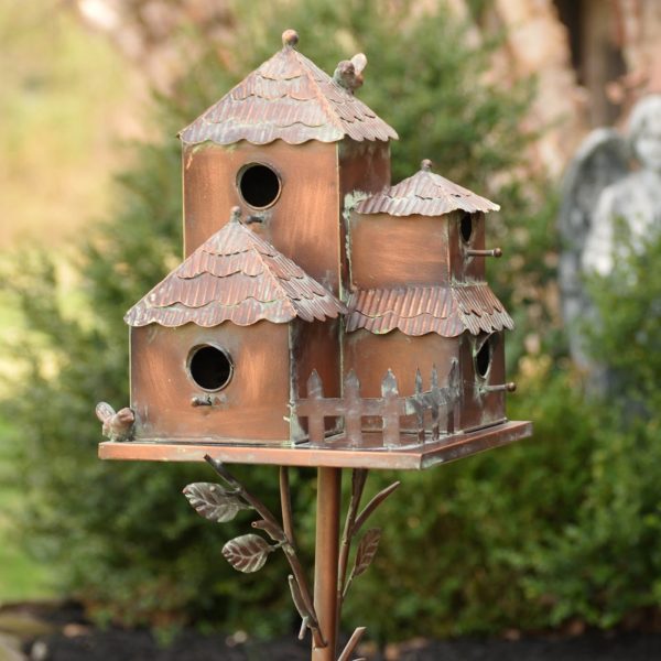 Side View of Metal Birdhouse Sitting on a Stake with fence and bird on top