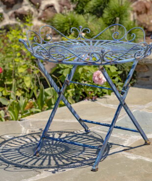 Victorian-style wrought iron folding garden table with X-shaped legs and filigree details in antique blue distressed finish in garden