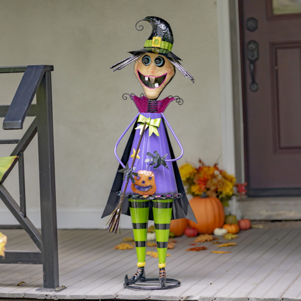 Halloween decoction of tall iron old witch standing figurine wearing purple and black cape standing on doorstep