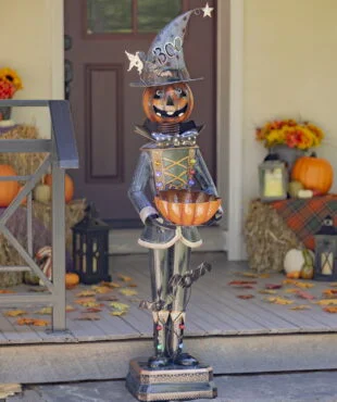 Halloween decoration of tall metal pumpkin soldier holding out orange candy bowl standing on door step