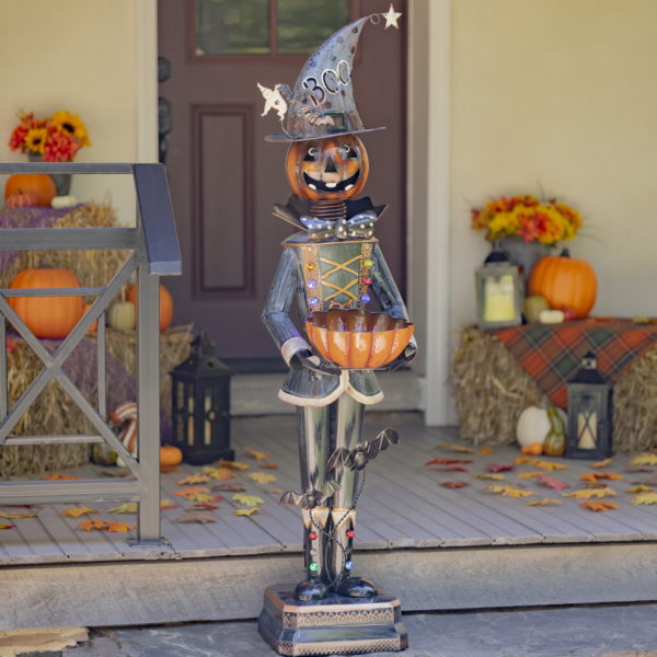 Halloween decoration of tall metal pumpkin soldier holding out orange candy bowl standing on door step