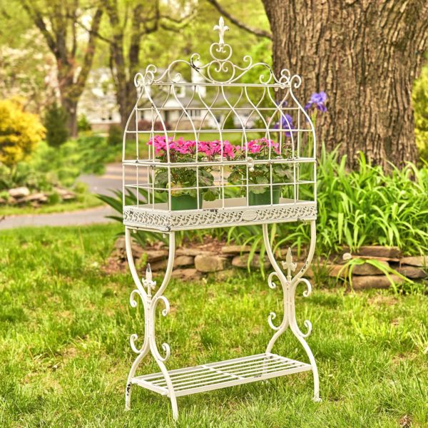 rectangular metal bird cage plant stand with fleur-de-lis details and shelf in antique white distressed finish with flower pots inside it
