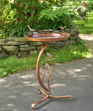 Iron shallow birdbath with branch stand on birds on the basin edge in copper finish standing in garden
