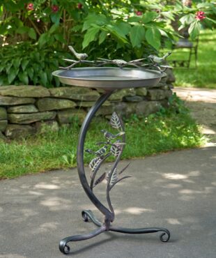 Galvanized iron shallow birdbath with branch stand on birds on the basin edge standing in garden