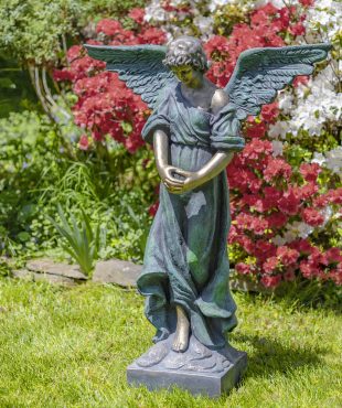 Antique bronze tall magnesium angel statue standing in a garden with her head bowed down holding her two hands together while her wings are spread wide open