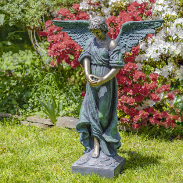 Antique bronze tall magnesium angel statue standing in a garden with her head bowed down holding her two hands together while her wings are spread wide open