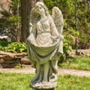 Antique grey tall angel magnesium statue holding up her dress creating a birdbath while a bird is perched at the edge of her dress and she is admiring it with two wings folded behind her