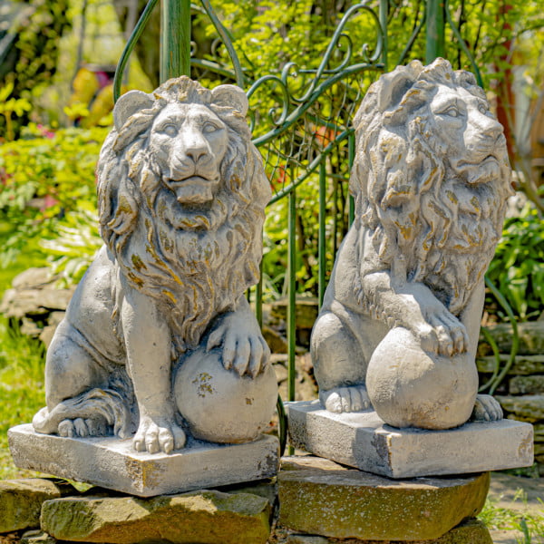 Set of 2 26.5 inches tall magnesium lion sentry statues with stone-like appearance in antique grey finish with a ball under a paw Marloni and Antonio on a fence in a garden