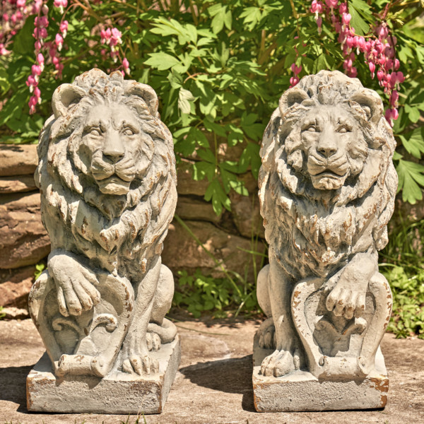 Two magnesium Lion statue in antique grey sitting upright with one of there paw cocked on a stone
