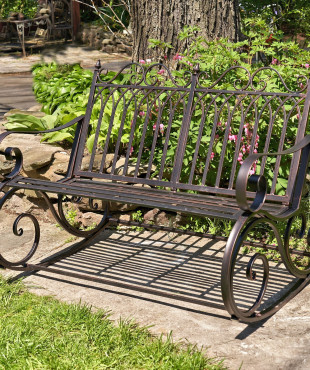 side view of Iron rocking bench with with filigree armrest and bottom part in antique bronze finish in garden