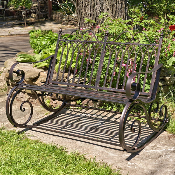 side view of Iron rocking bench with with filigree armrest and bottom part in antique bronze finish in garden