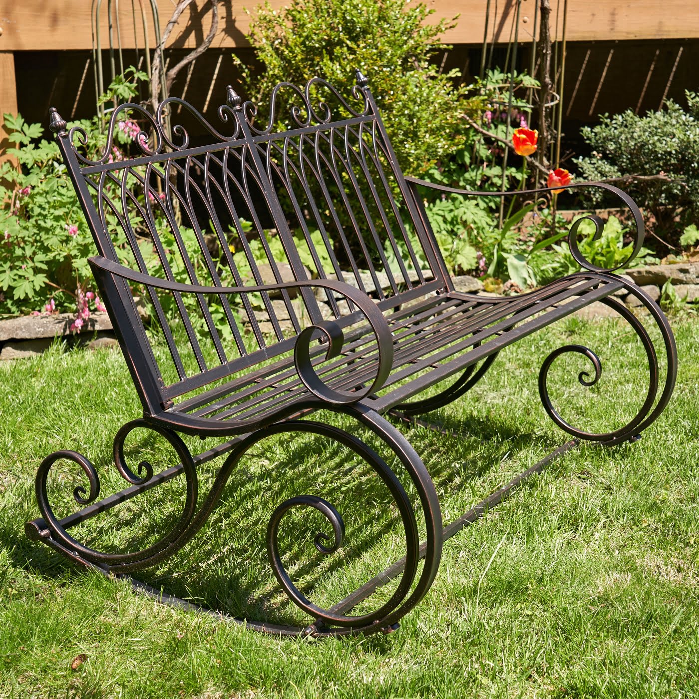 side view of Iron rocking bench with with filigree armrest and bottom part in antique bronze finish in garden