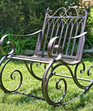 side view of Iron rocking chair with with filigree armrest and bottom part in antique bronze finish in garden