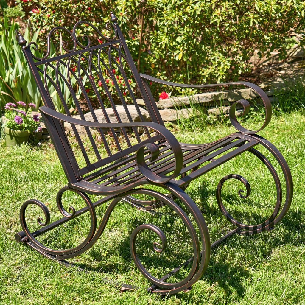 side view of Iron rocking chair with with filigree armrest and bottom part in antique bronze finish in garden