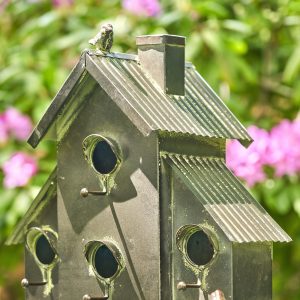 closed up image of galvanized metal multi-family birdhouse stake in a classic style with short chimney and little bird perched on top of it with patina accents
