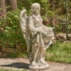 Side view image of Antique grey tall angel magnesium statue holding up her dress creating a birdbath while a bird is perched at the edge of her dress and she is admiring it with two wings folded behind her