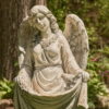 Close up image of Antique grey tall angel magnesium statue holding up her dress creating a birdbath while a bird is perched at the edge of her dress and she is admiring it with two wings folded behind her