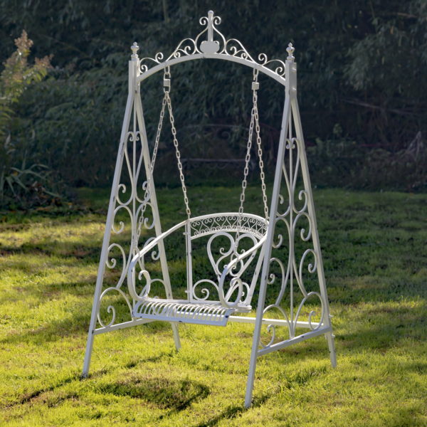 Full Angled View of White Iron wing Chair Hanging froma Chain with Scrolling Pattern throughout and heart like details on backrest