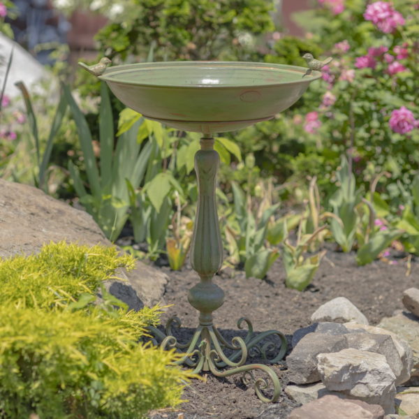 27 inch tall iron birdbath with hand painted distressed antique green finish, round basin with two small bird sculptures perched on the edge and decorative yet sturdy stand outside in flower garden