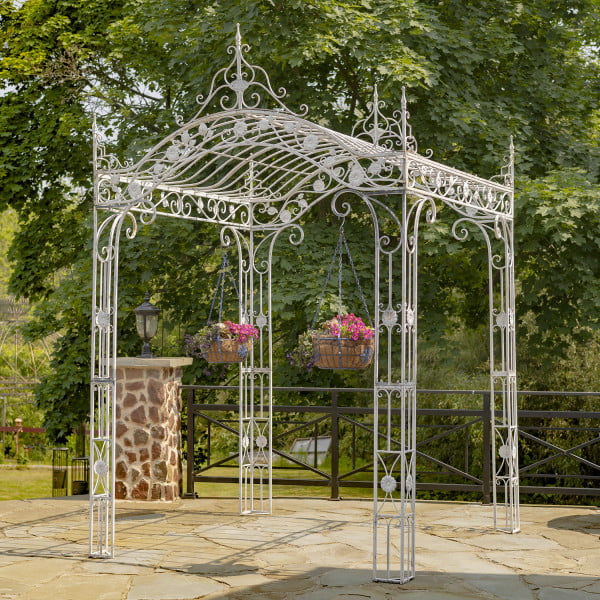 diagonal view 10.5 feet tall rectangular arched iron garden gazebo in antique white distressed finish in garden with two not included black iron hanging basket planters