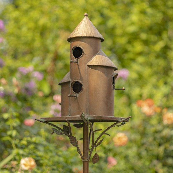Tall cylinder birdhouse stake in a copper color that has a cornicle roof with holes right around for birds and vines running from the stake to the birdhouse